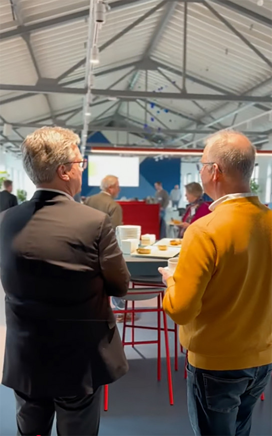 Foto: Menschen stehen bei einer Veranstaltung zusammen und unterhalten sich bei Kaffee und Snacks.