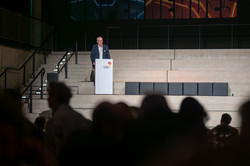 Photo: A person speaks at a podium on a stage.