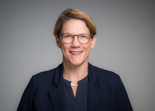 Portrait photo of Prof. Wiebke Möhring: Prof. Möhring wears a dark blue blouse and a dark blue blazer. She stands in front of a gray background and smiles at the camera.