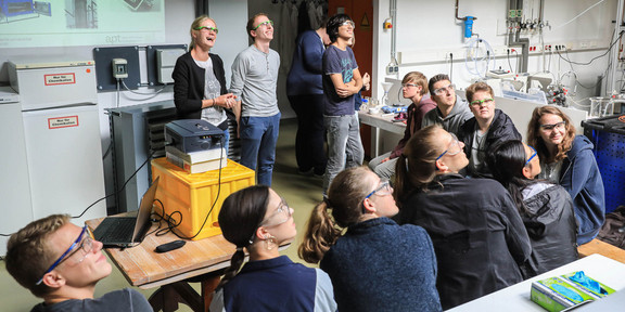 SchnupperUni Eine Gruppe Schüler*innen sitzt in einem Halbkreis vor drei präsentierenden Personen und einem Beamer. Alle Personen im Bild betrachten etwas außerhalb des rechten Bildrandes.