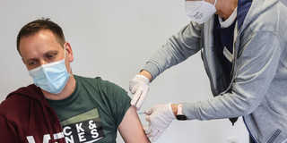 A female doctor gives a man an injection in the upper arm.