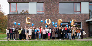 Eine Gruppe von Menschen, die goldene und blaue Luftballons in die Luft entlassen. Die goldenen Luftballons bilden das Wort "COPE"