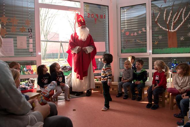Ein als Nikolaus steht in einem Raum umzingelt von Kindern aus der Kita.