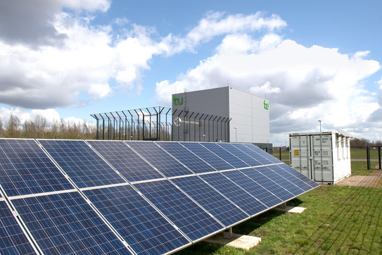 Photovoltaikanlage auf grünem Rasen mit Wolken am Himmel.