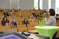 Frau Szymanski steht an einem grünen Tisch mit TU-Logo vor einem recht gut besetzten Hörsaal.