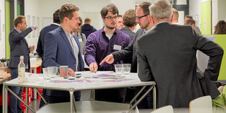 Four men standing around a round table talking