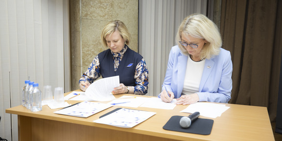 Two women sit at a desk and sign documents