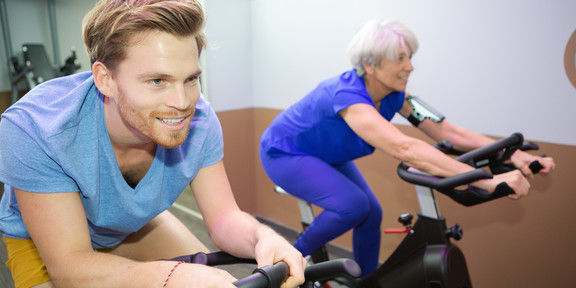 Sport Eine ältere Frau und ein junger Mann sitzen nebeneinander auf Spinning-Fahrrädern.