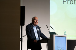 A man stands at a lectern in front of a power point presentation.