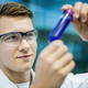 Student mit Schutzbrille betrachtet Röhrchen mit blauer Flüssigkeit