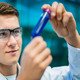 Student mit Schutzbrille betrachtet Röhrchen mit blauer Flüssigkeit