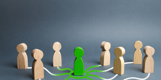 Seven small wooden figures stand around a green figure. The wooden figures are connected to the green one by white lines.