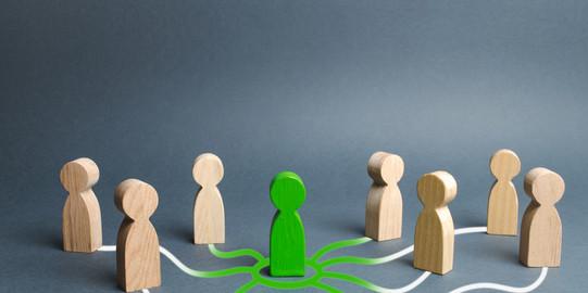 Seven small wooden figures stand around a green figure. The wooden figures are connected to the green one by white lines.