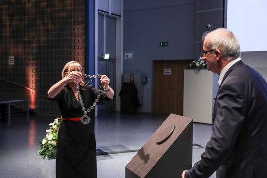 Professor Ursula Gather hands new President Professor Manfred Bayer the chain of office. They both stand on a stage.