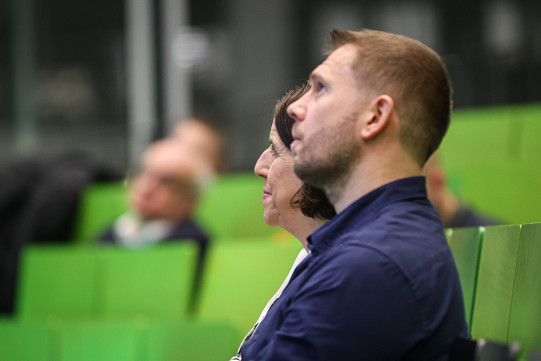 im Vordergrund zwei Hörende, im Hintergrund Hörsaal mit weiterem Publikum