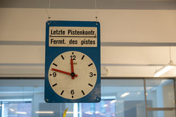 Blaues Schild mit einer weißen Uhr und schwarzer Schrift.