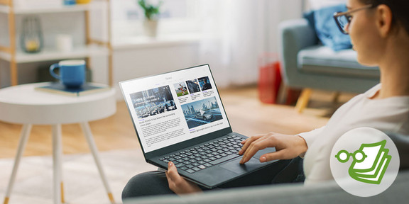 Eine junge Frau sitzt auf einem Sessel während sie an ihrem Laptop im Internet surft.