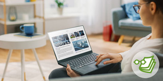 Eine junge Frau sitzt auf einem Sessel während sie an ihrem Laptop im Internet surft.