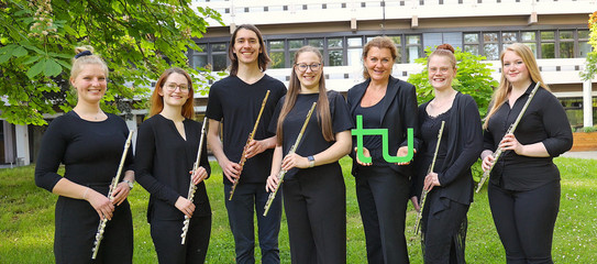 TU Flutes Gruppenbild des Ensembles "TU Flutes", die Musiker*innen halten ihre Flöten in der Hand, die Leiterin hält ein grünes TU-Logo in der Hand.
