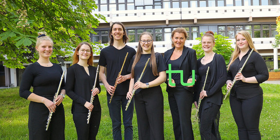 TU Flutes Gruppenbild des Ensembles "TU Flutes", die Musiker*innen halten ihre Flöten in der Hand, die Leiterin hält ein grünes TU-Logo in der Hand.