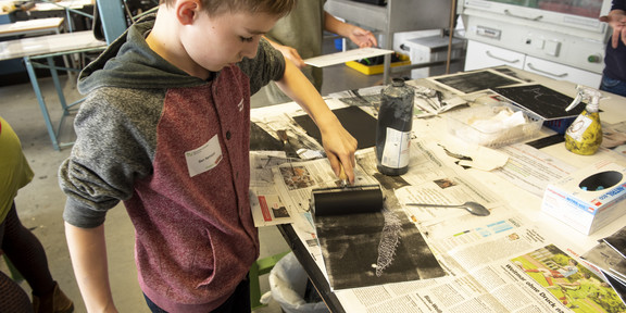 A boy works with black paint and a paint roller.