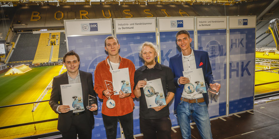 Four trainers stand side by side in Signal Iduna Park, holding a certificate in their hands.