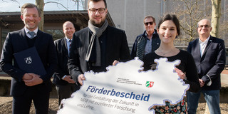 Mehrere Personen stehen draußen in einem Kreis und halten ein Schild.