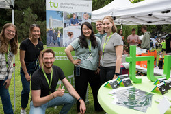 mehrere TU-Mitglieder stehen an einem Stand und lächeln in die Kamera