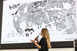 Eine Frau mit blonden Haaren präsentiert einen Grundriss einer Stadt.