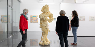 Ausstellung Goldenes Wunder Drei Frauen stehen um eine Skulptur und betrachten diese.