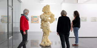 Drei Frauen stehen um eine Skulptur und betrachten diese.