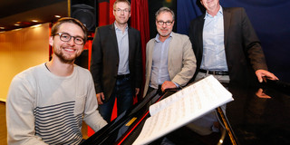 Gruppenfoto von vier Männern, von denen einer am Klavier sitzt