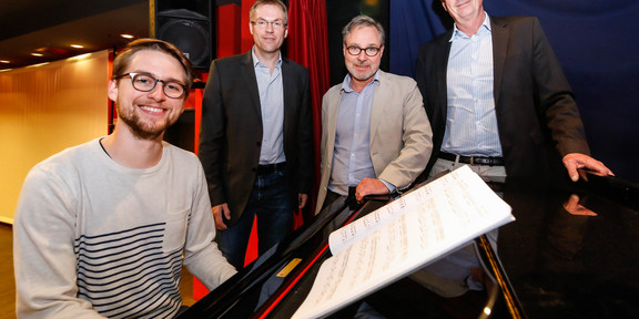 tuconcept Gruppenfoto von vier Männern, von denen einer am Klavier sitzt