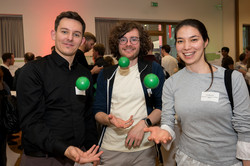 Two men and a woman are tossing a small green ball into the air while smiling at the camera.