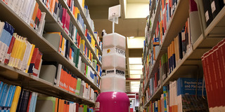 Ein Serviceroboter steht zwischen zwei Bücherregalen in der Universitätsbibliothek.