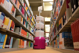 April Ein Serviceroboter steht zwischen zwei Bücherregalen in der Universitätsbibliothek.