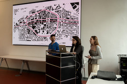 Three people present a city map at a podium in front of an audience.