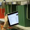 The image shows a tablet with a glowing screen held in a row of books in the library.