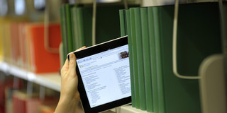 Open Access The image shows a tablet being pulled out from a row of books in the library.