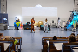 Drei Personen stehen während der DLR_Raumfahrt_Show im vollbesetzten Audimax. Sie sind verkleidet als Astronautin, als Känguru und als Erde.