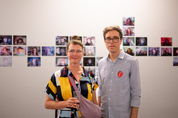 Zwei Personen stehen vor der Ausstellung und schauen in die Kamera.