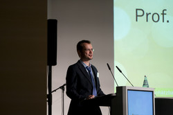 A person stands at the lectern in front of a power point presentation.