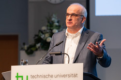 Ein Mann steht an einem Pult, an dessen Front technische universität dortmund steht.