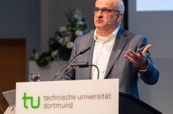 Ein Mann steht an einem Pult, an dessen Front technische universität dortmund steht.