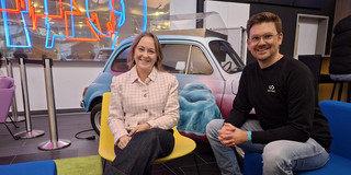 Foto: Michelle Twardzik und Dr. Thomas Seidensticker sitzen in auf einer blauen Couch und einem gelben Stuhl und lächeln in die Kamera.