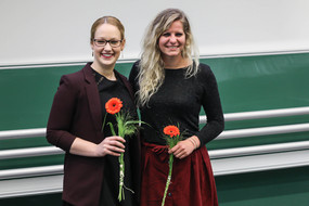 Zwei lächelnde Absolventinnen mit roten Blumen in der Hand.