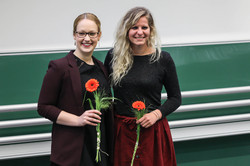 Zwei lächelnde Absolventinnen mit roten Blumen in der Hand.
