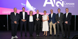 Group photo with eight people on a stage, with AI24 in the background