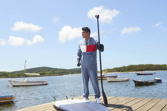 Das Werbefoto der Marke Tommy Hilfiger zeigt ein männliches Model mit Armprothese auf einem Holzsteg am Ufer eines Sees. In der Hand hält er ein Paddel.  