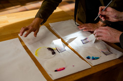 Ein Tisch mit Papiertüchern, auf welche schwarz-bunt bemalte Papierkreise gemalt werden